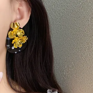 Detailed close-up showing the intricate gold floral design on a black resin oval stud earring