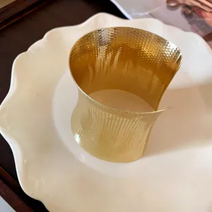 Detail view of a golden hammered metal open cuff bracelet on a white ceramic plate.