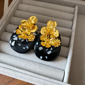 Detailed view of elegant gold metal flower accents on black resin oval stud earrings