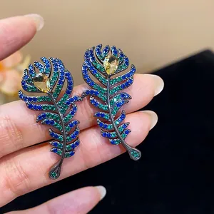 Close-up detail of feather-shaped earrings with colorful sparkling blue and green zircon