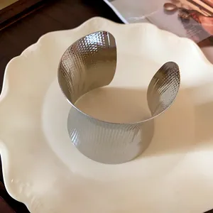 Detailed view of a wide silver-colored metal cuff bracelet with hammered texture on a plate.