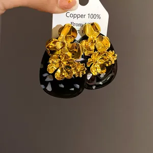 Close-up of vintage-style oval resin earrings with ornate gold-colored metal flowers.