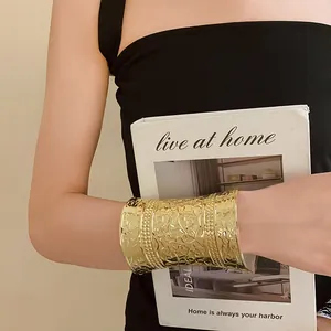 Close-up of ornate gold embossed metal wide cuff bracelet featuring vintage floral patterns.