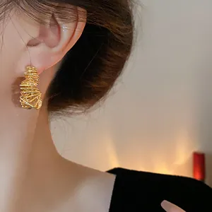 Close-up of gold-plated irregular wire earrings worn on the ear for a luxury fashion look