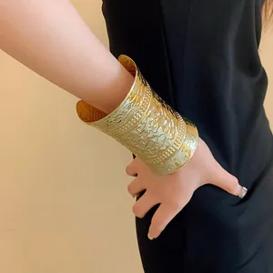 Close-up detail of a wide gold metal cuff bracelet with intricate floral engraved patterns