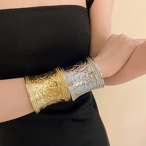 Detailed view of ornate gold and silver metal open cuff bracelets on model arm