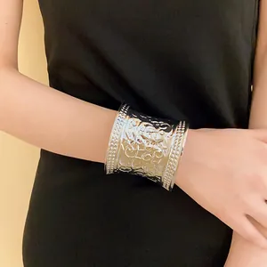 Close-up view of a silver-tone metal cuff bracelet with intricate engraved patterns.