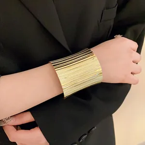 Close-up of wide gold metal cuff bracelet with textured stripes on model's wrist
