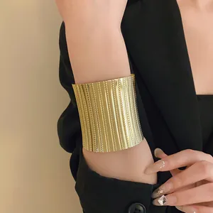 Detailed close-up of wide golden metal open cuff bracelet with textured stripe pattern