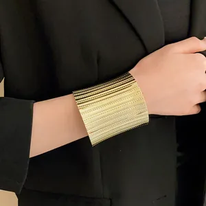 Close-up of a wide gold metal open cuff bracelet with horizontal textured grooved design.