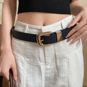 Detail shot of a wide navy belt with a polished gold-tone buckle worn on white pants