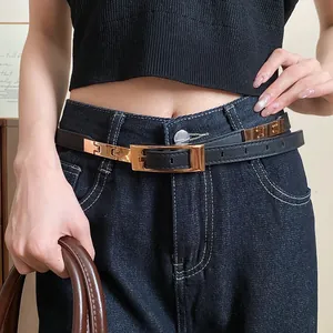 Detail of a western-style black leather belt with gold buckle worn on denim jeans