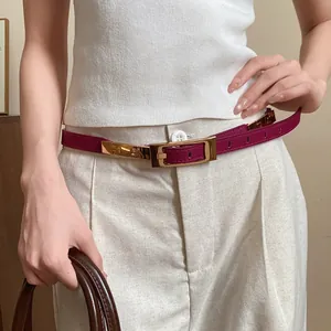 Close-up of a slim magenta leather belt with a gold buckle on a model's waist.