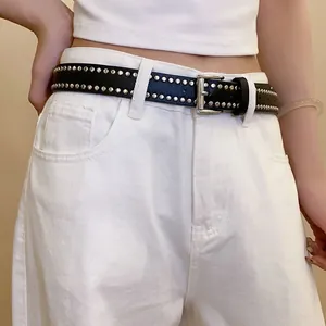 Close-up detail of western style black leather belt with silver rivets on white jeans.