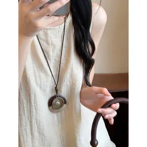 Detailed macro shot of Zen-style long necklace featuring a circular bird pendant and wooden accents