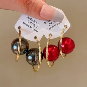 Close-up of geometric gold-finish hoop earrings with large red and gunmetal sphere beads