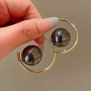 Close-up of geometric gold hoop earrings with dark grey metallic pearls detail