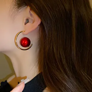 Close-up of dramatic geometric hoop earrings with a large red pearl on an Asian model.
