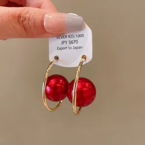 Close-up of gold hoop earrings with large vibrant red pearls on a white tag