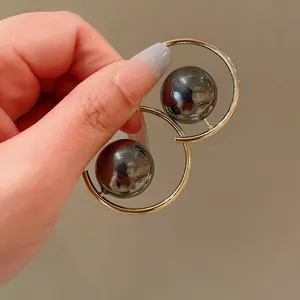Close-up of geometric gold hoop earrings with dark metallic pearls held by hand