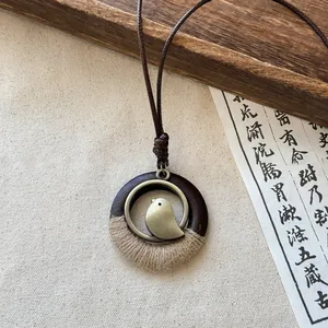 Detailed view of a Zen-style bird pendant necklace featuring wood, metal, and jute.