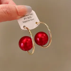 Detail shot of gold hoop earrings featuring large glossy red pearls and silver needle