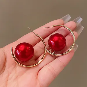 Macro detail view of elegant gold hoop earrings featuring large glossy red beads held in hand.