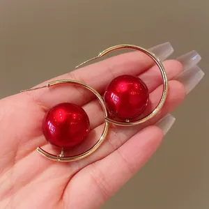 Detailed close-up view of geometric gold hoop earrings featuring large glossy red pearl beads