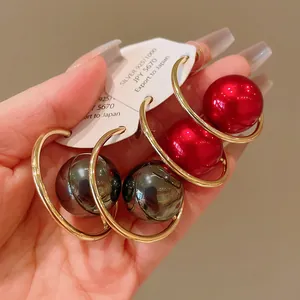 Close-up detail of oversized gold hoop earrings with glossy red and grey pearls