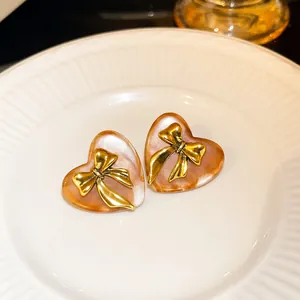 Close-up of vintage brown heart earrings with golden bow detail on a white ceramic plate.