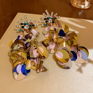 Close-up of oversized sequin earrings with colorful rhinestones and gold leaf details.