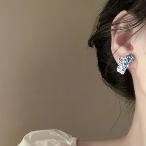 Close-up macro view of a blue organic shaped enamel stud earring worn on a model ear