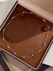 Detailed view of a vintage gold chain necklace with blue beads presented in a brown jewelry box