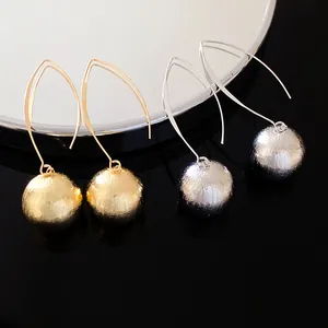 Macro view of textured gold and silver sphere pendant earrings on black reflective surface