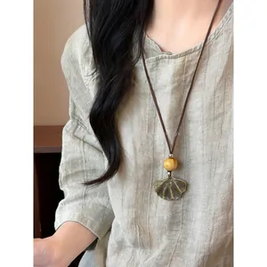 Detail view of a Neo-Chinese ginkgo leaf pendant necklace on a linen shirt
