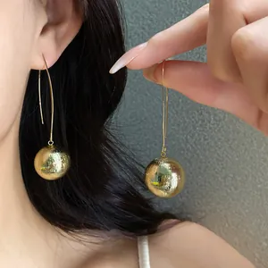 Close-up detail of stylish golden textured spherical dangle earrings worn by a model