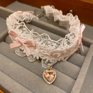 Dettaglio del ciondolo a cuore in cristallo rosa su un choker di pizzo bianco
