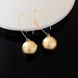 Macro view of gold textured spherical pendant earrings with long elegant ear hooks
