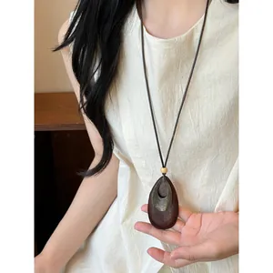 Close-up detail of a Zen-style long necklace with teardrop wood pendant worn on model