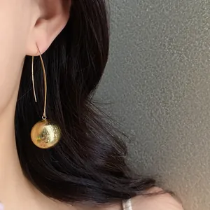 Detailed view of gold textured sphere earrings with elegant long hooks worn by a model