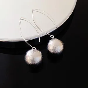 Macro view of textured silver sphere pendant earrings with minimalist long hook design