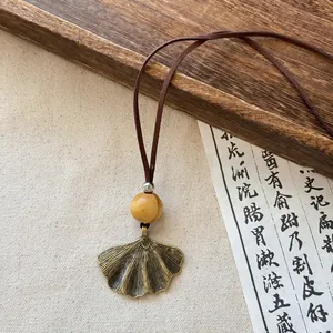 Detailed view of a retro brass ginkgo leaf pendant on a brown long cord necklace