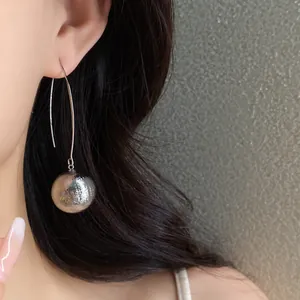 Close-up detail of a silver textured sphere pendant earring worn on an ear with dark hair