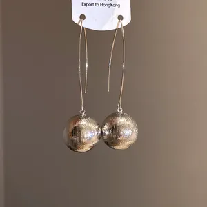 Close-up detail of large silver spherical drop earrings with a brushed textured finish.