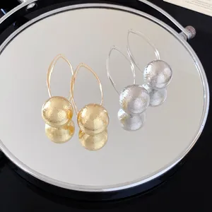 Close-up detail of gold and silver textured ball drop earrings on a reflective mirror.