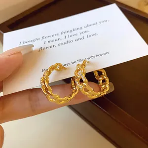 Gros plan de boucles d'oreilles créoles chaîne dorées avec zircons sur une carte.