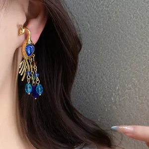 Detalle de pendiente de pavo real dorado con gemas azules usado en la oreja