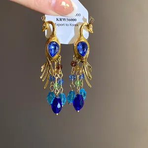 Exquisitos pendientes de pavo real dorados con cristales azules y borlas de cuentas.