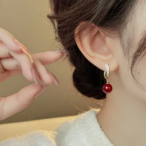 Close-up of elegant gold earrings with red round bead and zircon accents on model