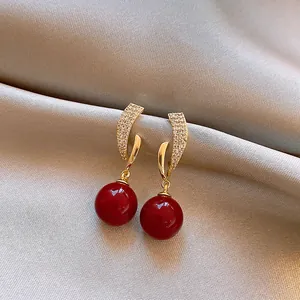 Close-up of golden geometric earrings with pavé zircons and red spherical drops.